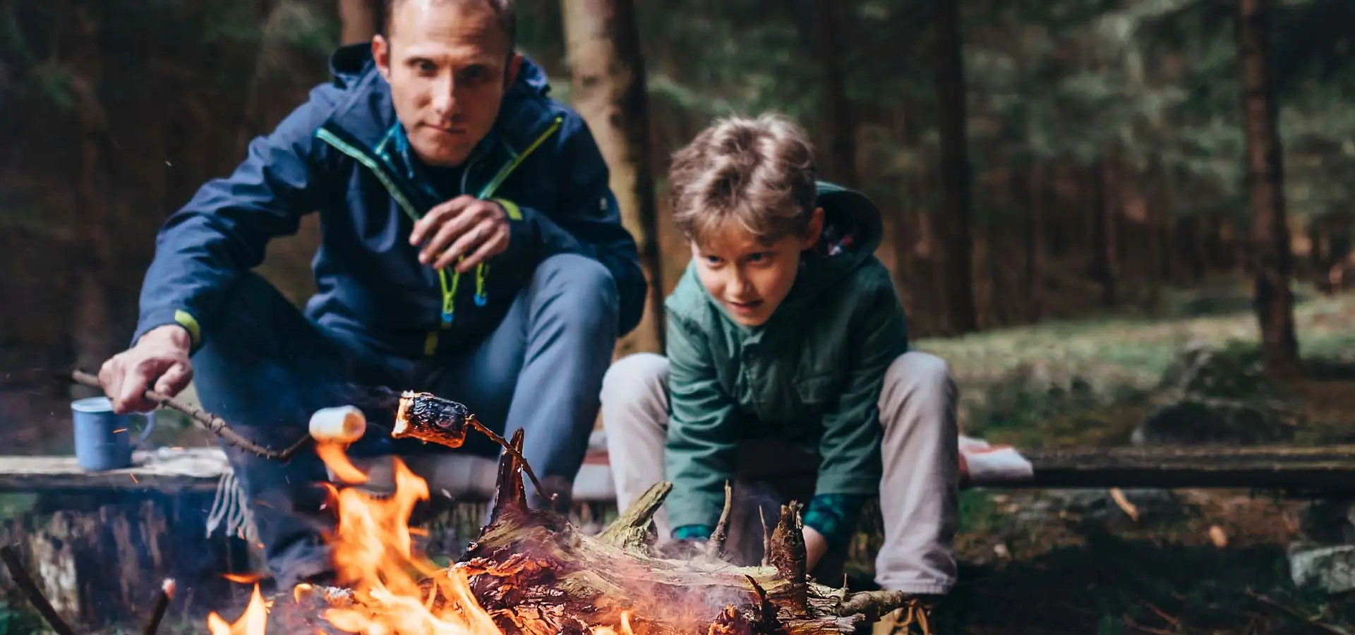 A man and a child making s'mores on a bonfire.